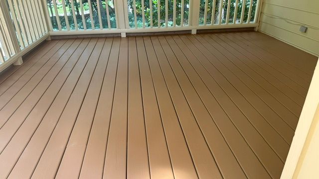 Wooden deck painted brown, surrounded by white railing and a yellow house.