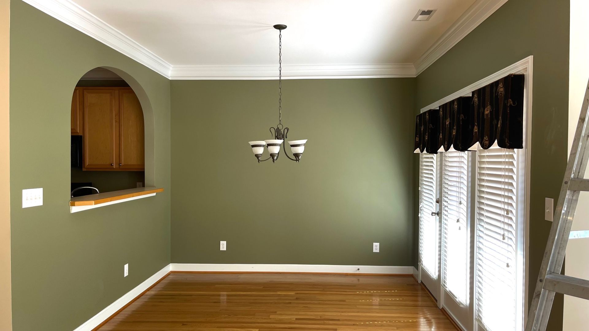 Green dining room with archway, chandelier, and french doors with shutters.