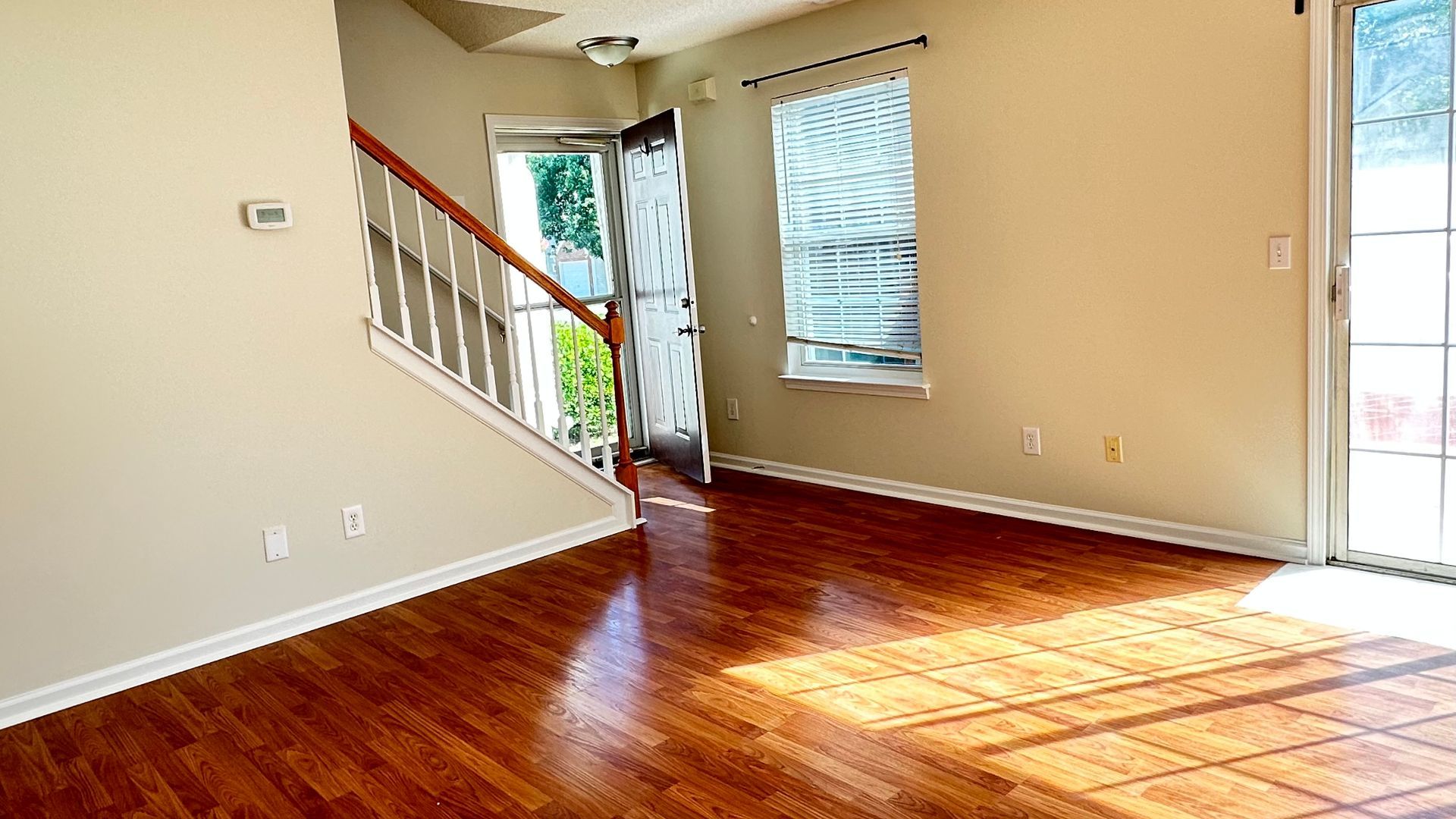 Empty interior room with hardwood floors, stairs, and natural light from doorway and window.
