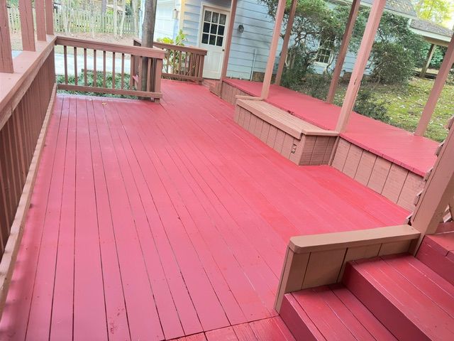 Red-painted wooden deck with built-in seating, stairs, and railing, with a glimpse of a house and yard.