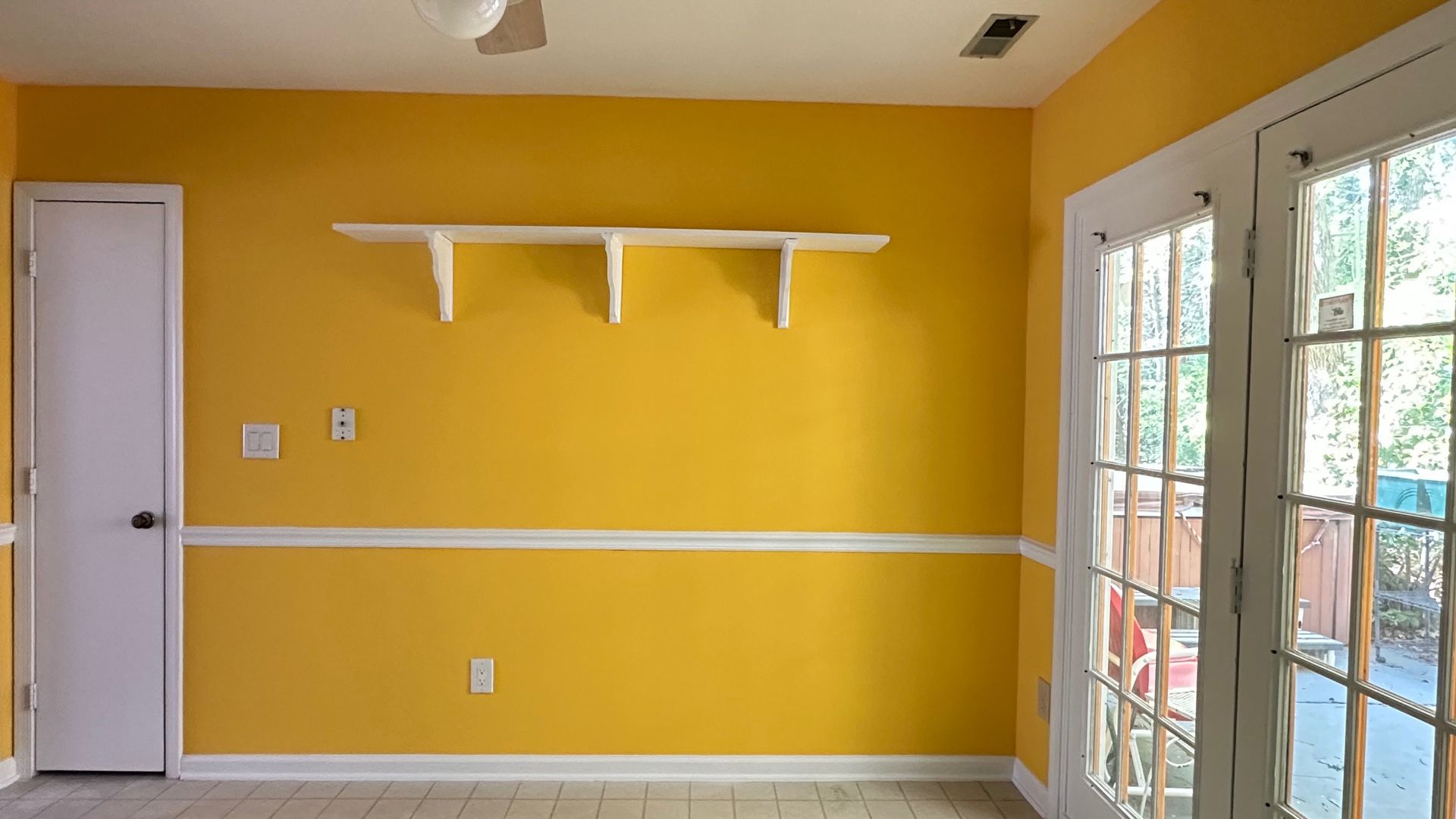 Yellow-painted room with white trim, a door, and French doors leading outside; a white shelf is on the wall.