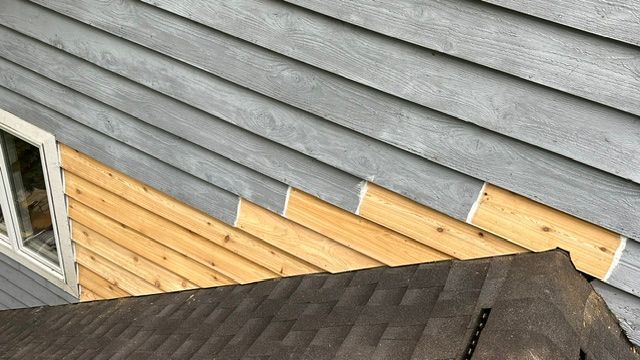 Gray siding and new cedar siding on a house, with a brown shingled roof below.