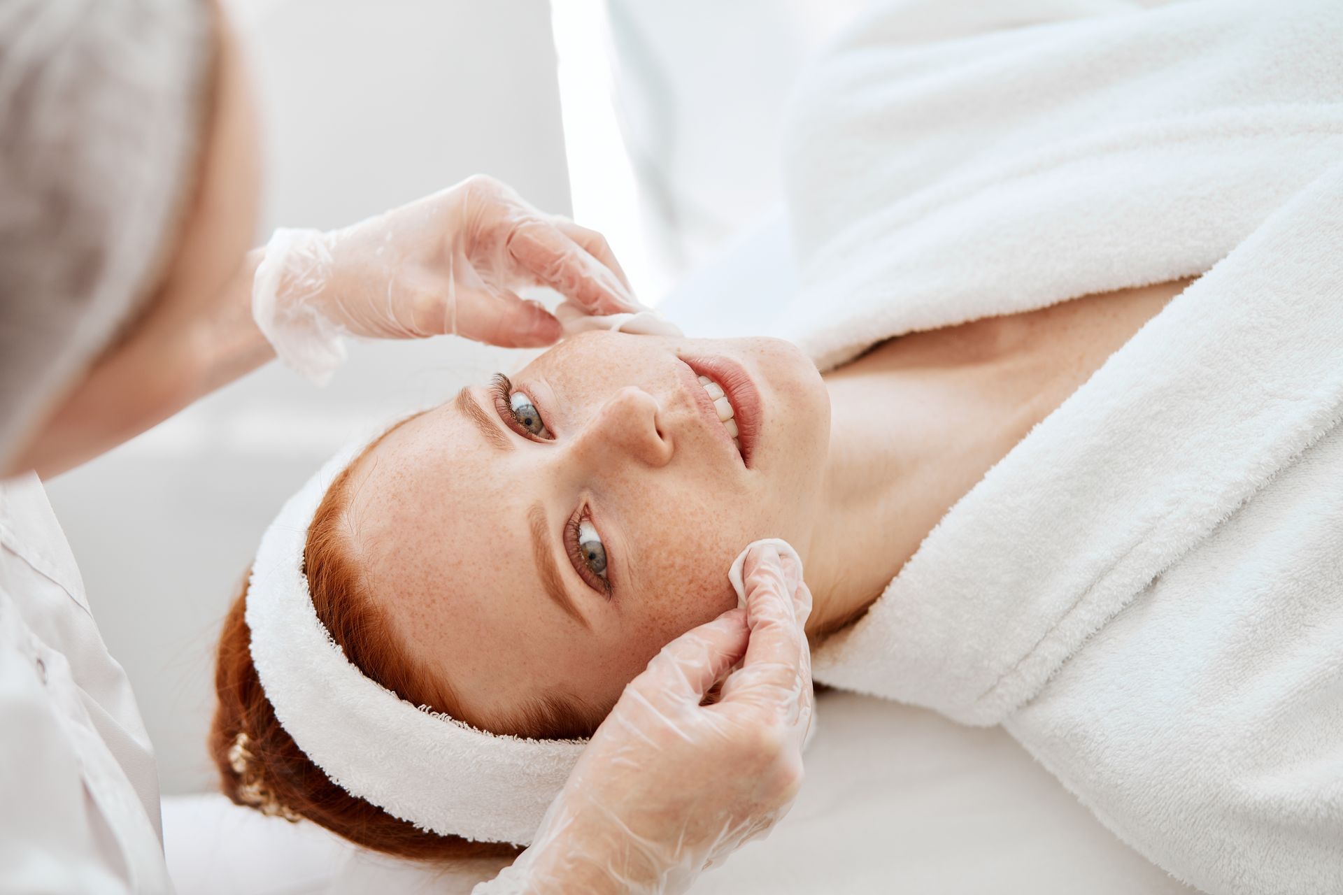 Esthetician gently touching woman's face during a skincare facial treatment.