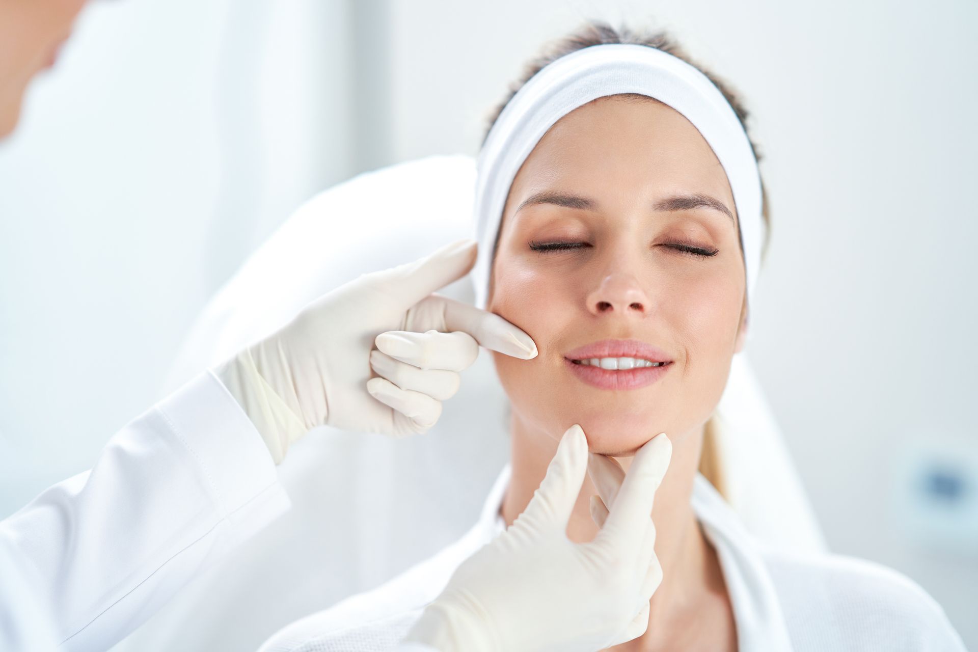 Gloved medical professional examining a patient’s face during a skincare consultation. Gloved medical professional examining a patient’s face during a skincare consultation.
