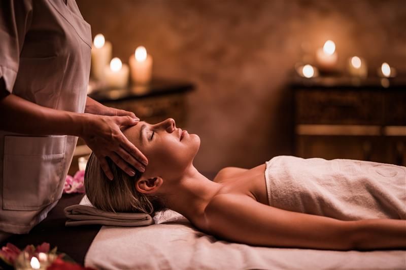 Spa therapist providing relaxing head massage in a candlelit treatment room.