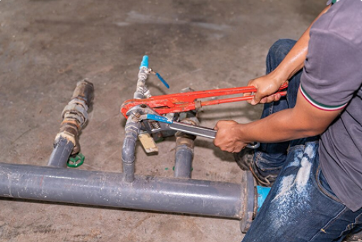 Plumber using wrenches to repair pipes in a concrete setting.