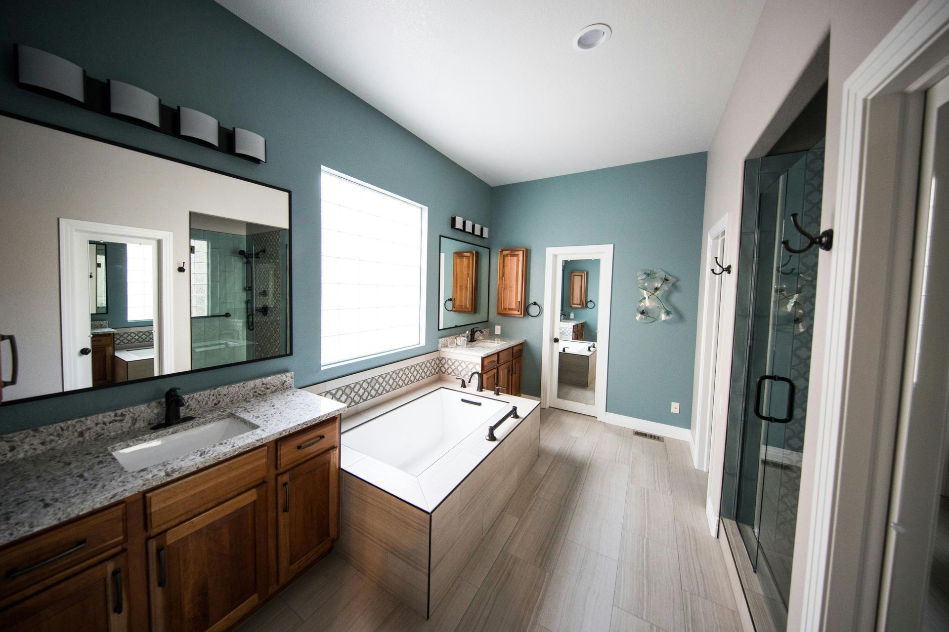 Spacious bathroom with a bathtub, two sinks, and a shower. Blue walls, wood cabinets, and light flooring.