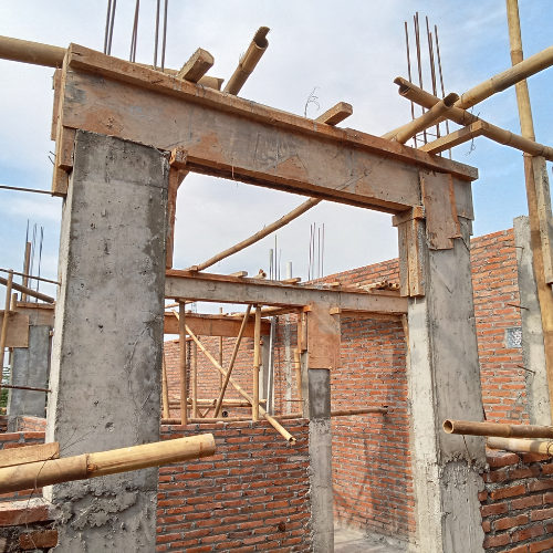 Electrician in a yellow hard hat and overalls working on wiring near a window.