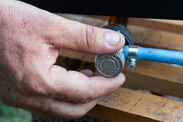 A hand turning a small metal valve connected to a blue hose, likely to control fluid or gas flow.
