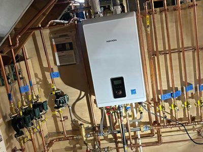 A wall-mounted white Navien boiler surrounded by a complex network of copper pipes in a mechanical room.