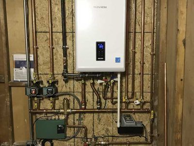 Navien wall-mounted tankless water heater with complex copper piping and electrical controls on a wooden wall.