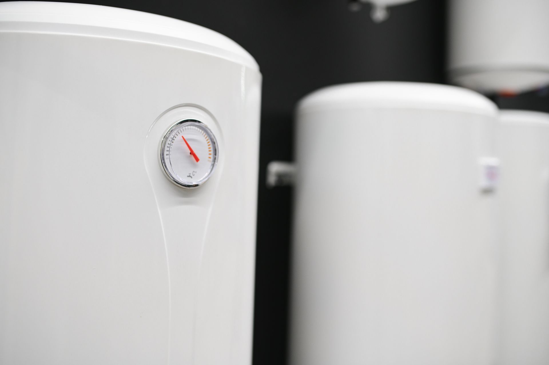 White, cylindrical electric water heaters with a circular temperature gauge on the foreground unit.