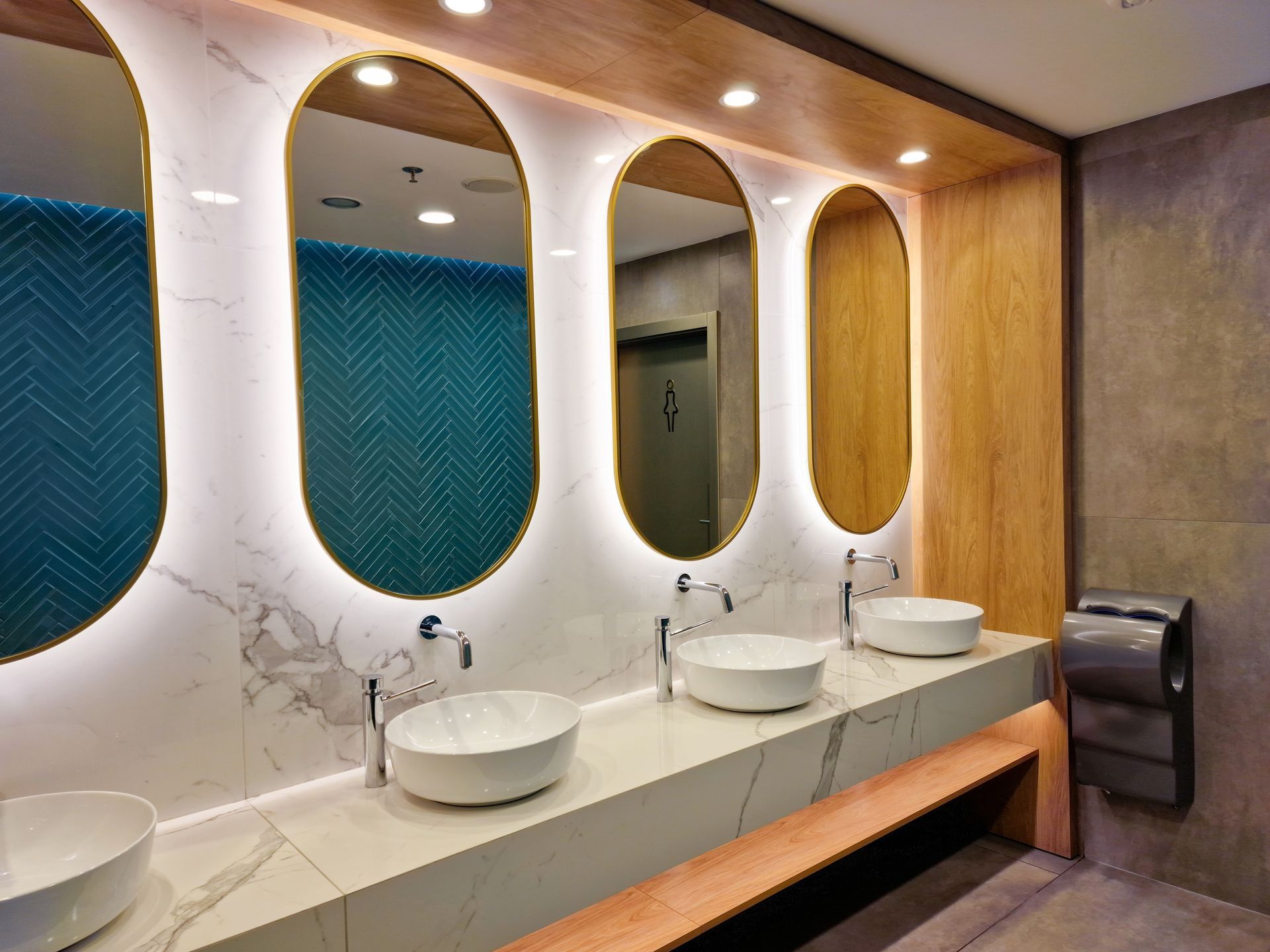 A modern bathroom vanity with marble walls, three oval mirrors with backlit edges, and white vessel sinks.