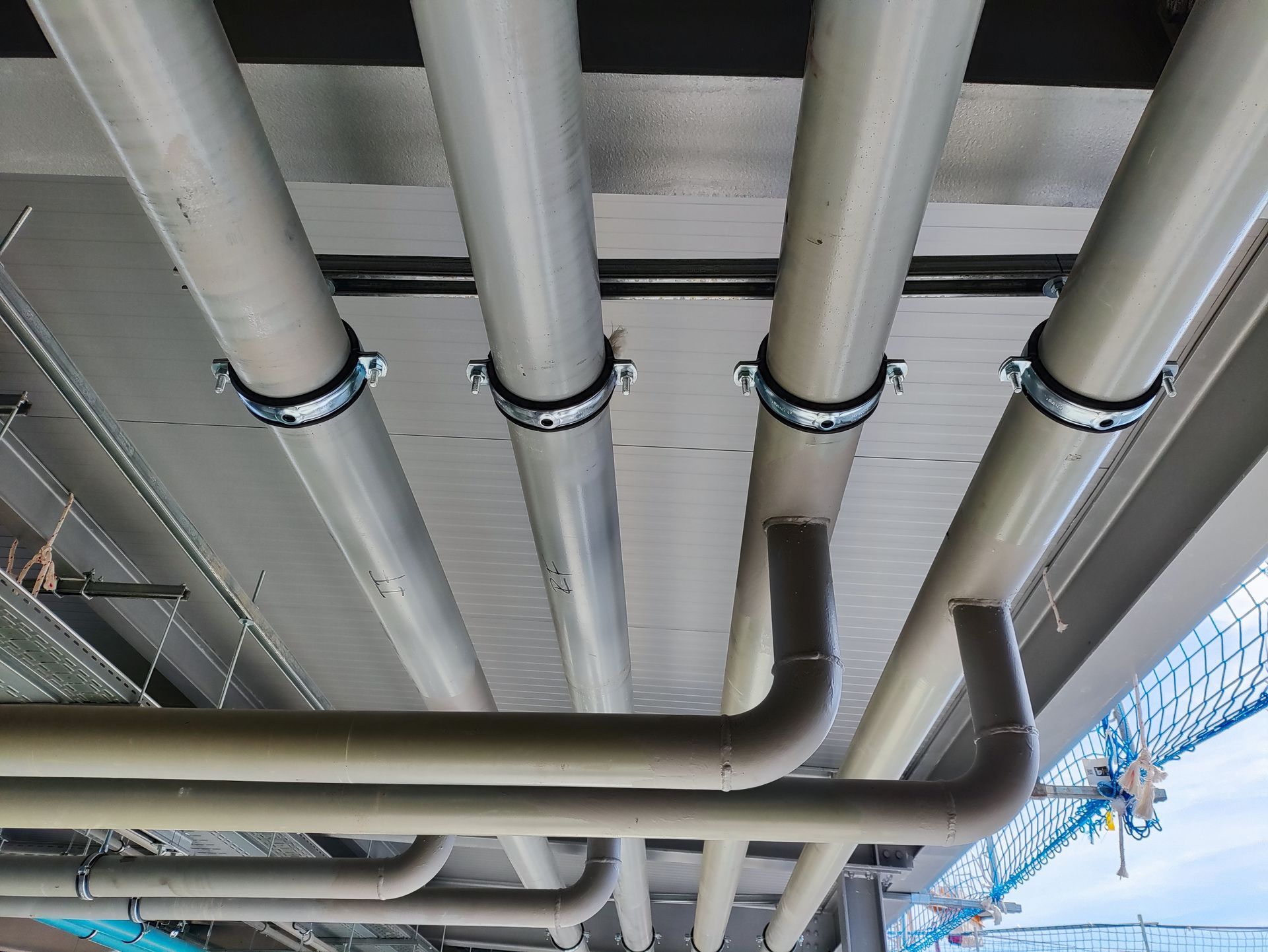 A low-angle shot of grey utility pipes mounted to a textured ceiling, showing both vertical and horizontal runs.