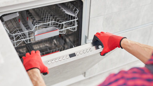 A man wearing red gloves is opening a dishwasher door.