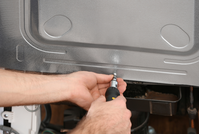 A man is fixing a refrigerator with a screwdriver.