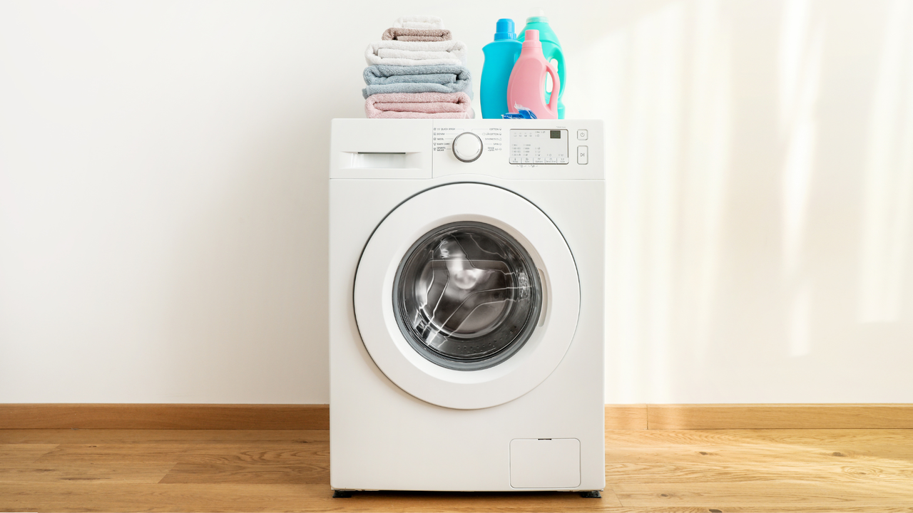 A white washing machine with a stack of clothes on top of it.