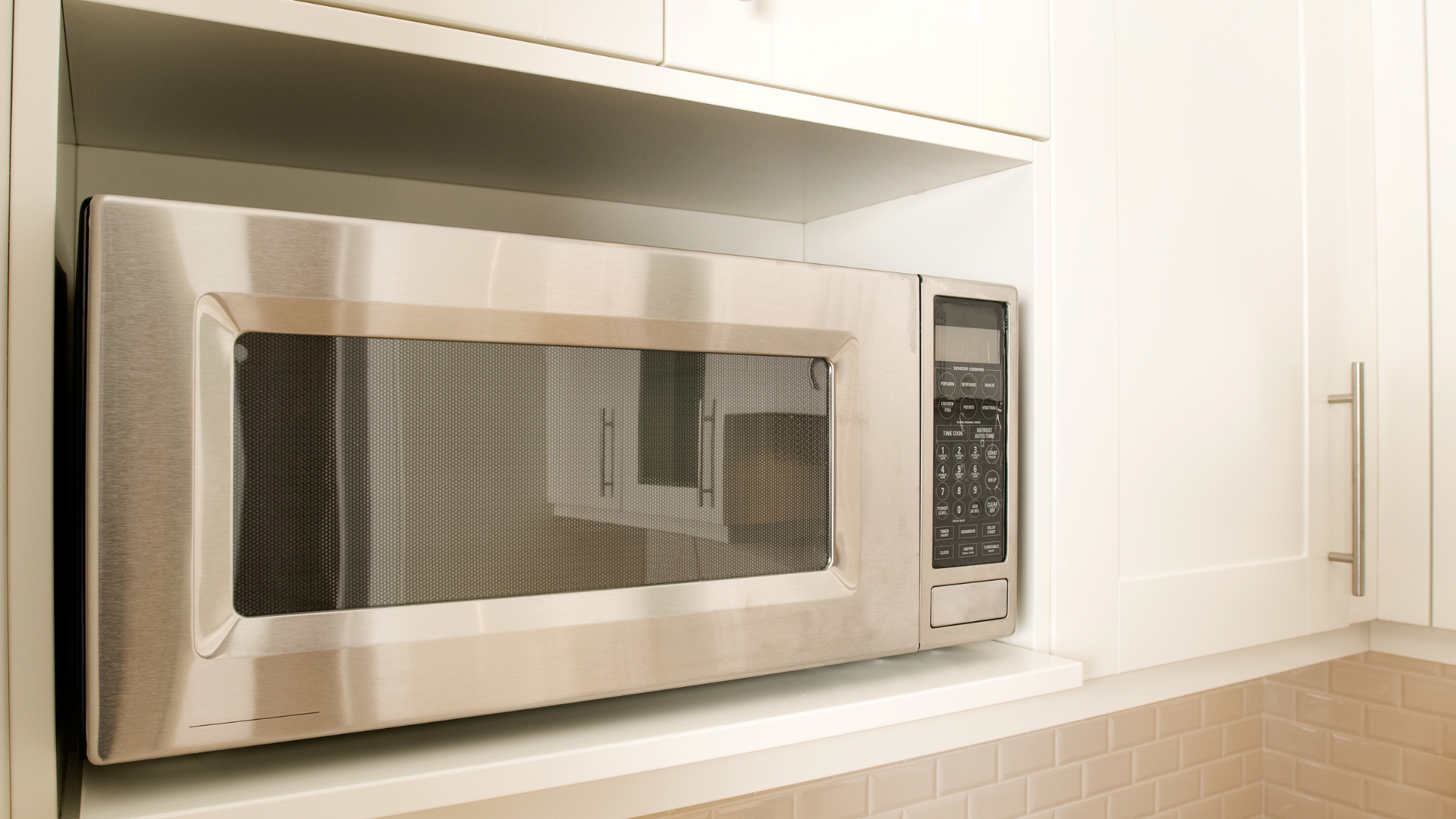 A stainless steel microwave is sitting on top of a shelf in a kitchen.
