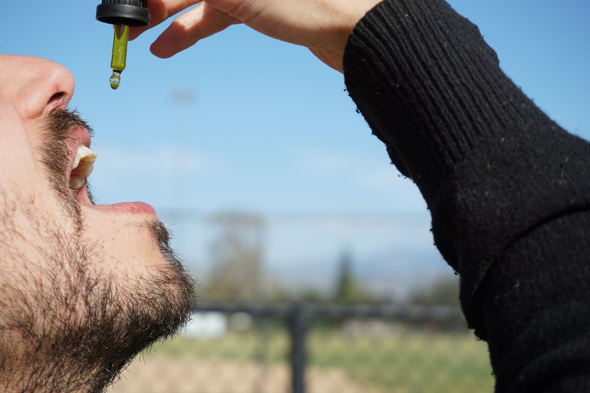 A person receives drops from a dropper into their mouth against a bright sky background.