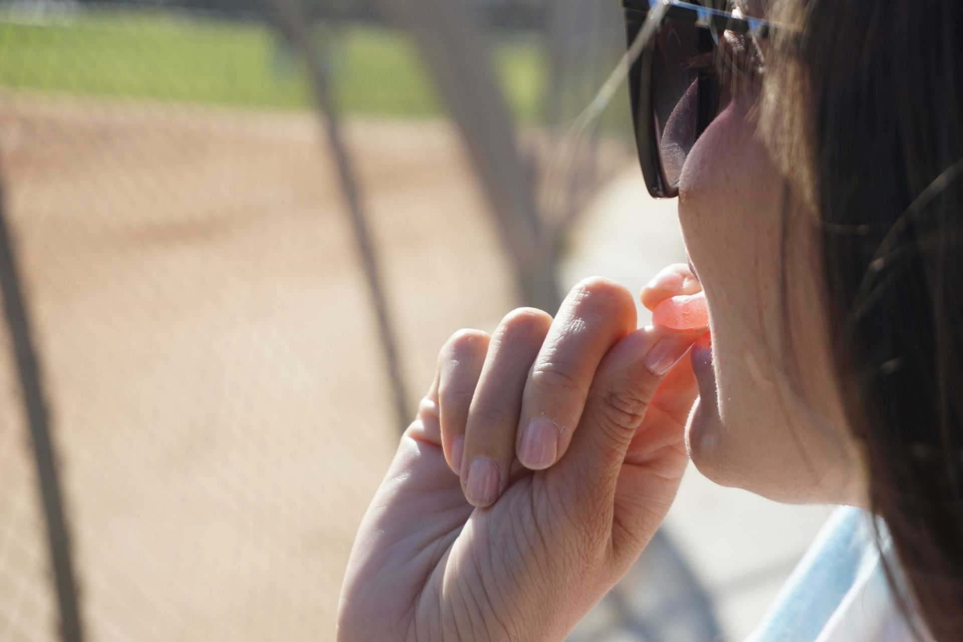 Woman biting fingernail, wearing sunglasses, overlooking a baseball field.