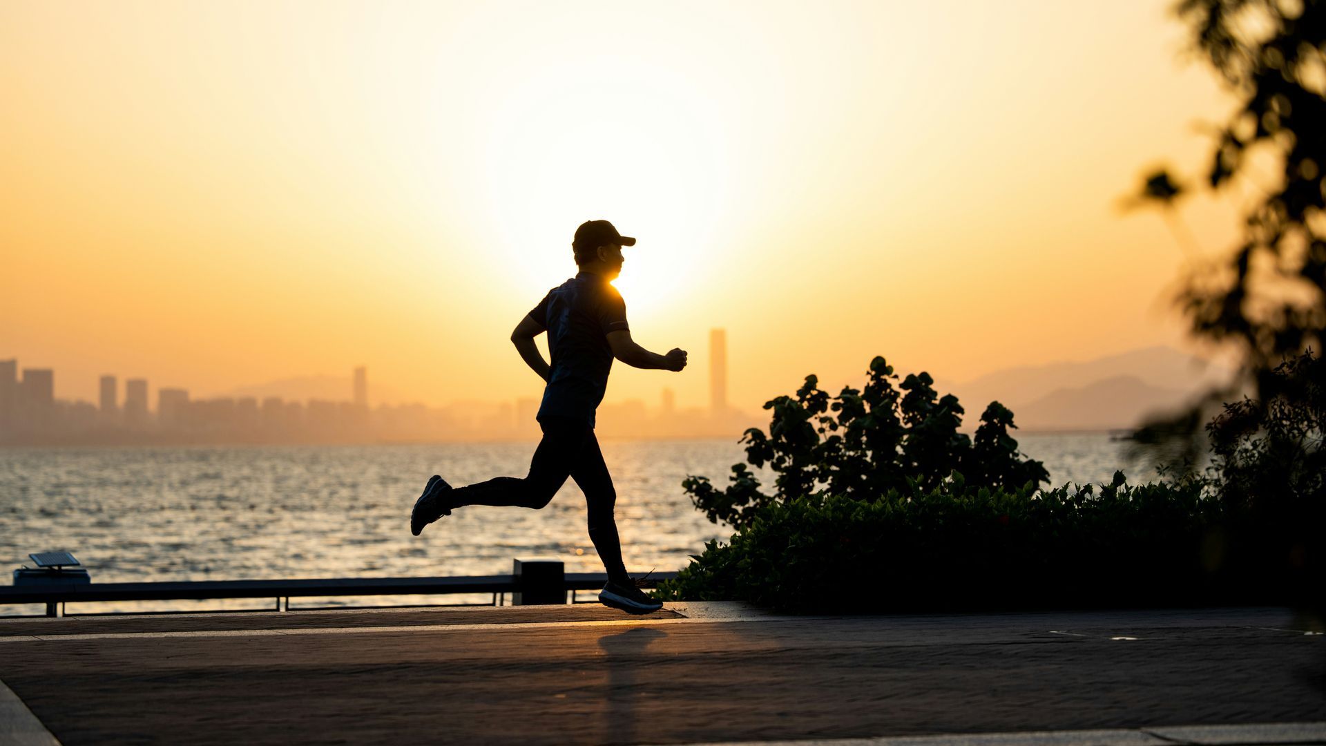 Silhouette of a person running along a waterfront at sunset.