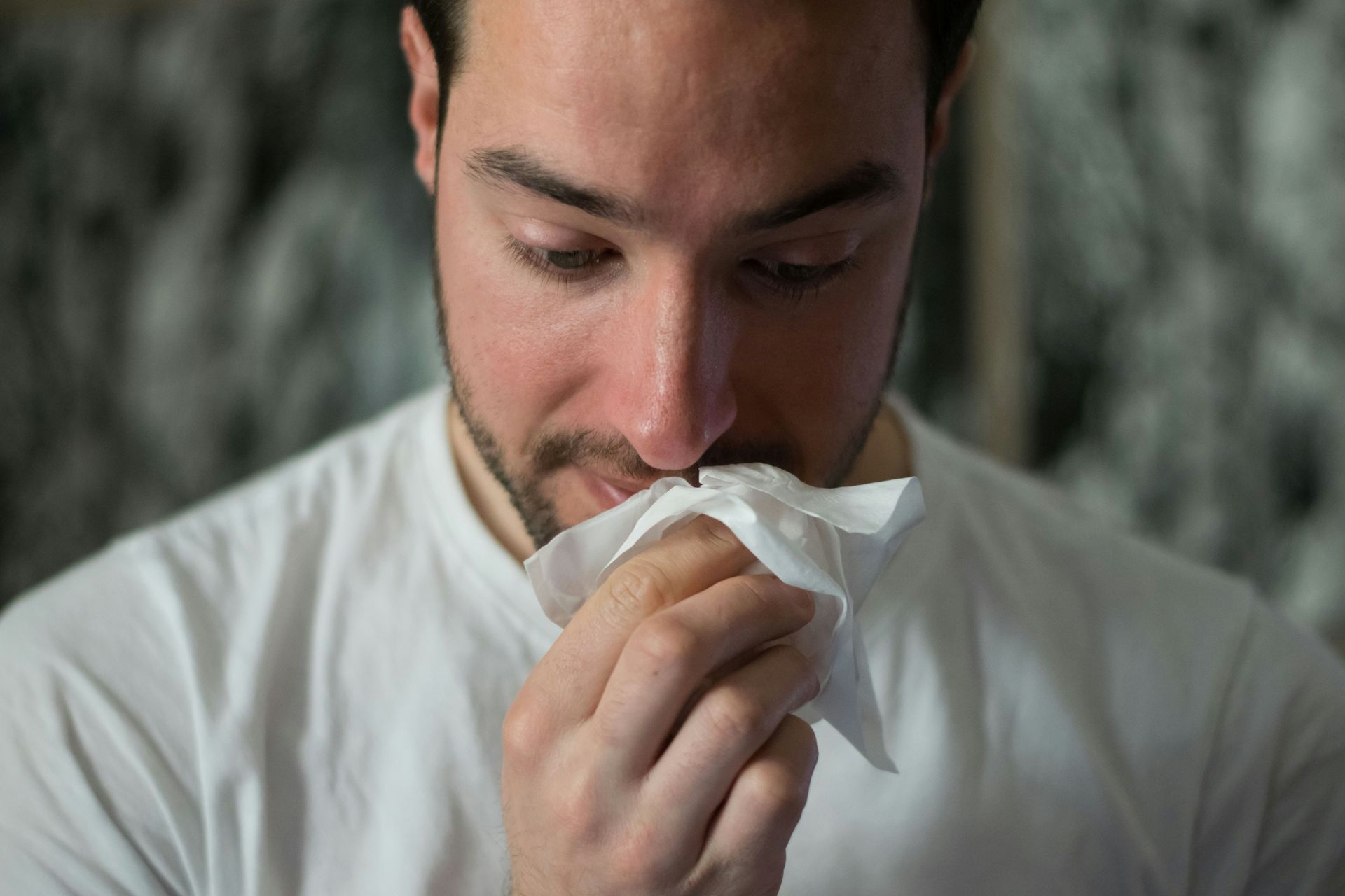 Man in white shirt blowing his nose with a tissue.
