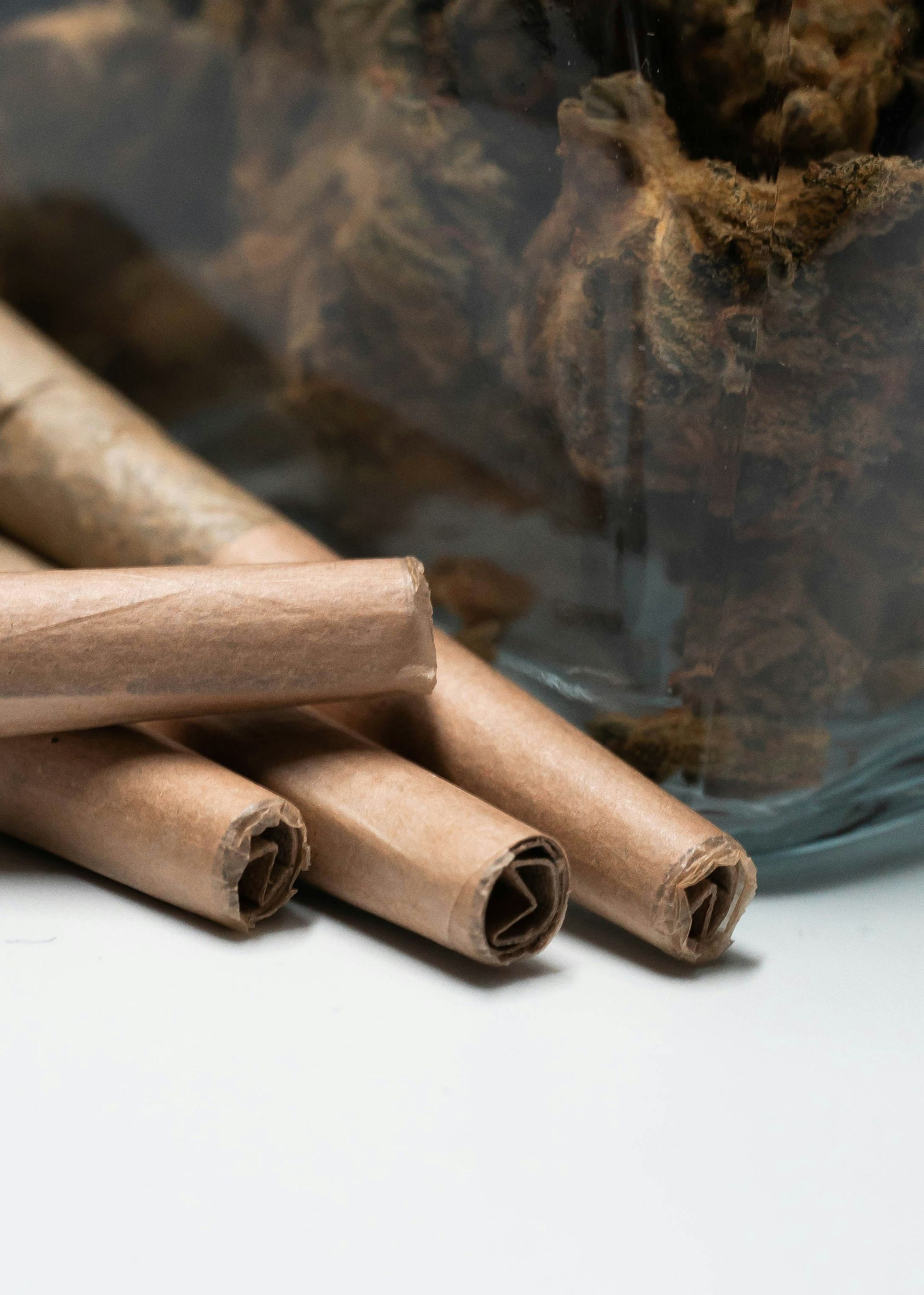 Four brown rolled cigarettes next to a glass jar filled with similar material.