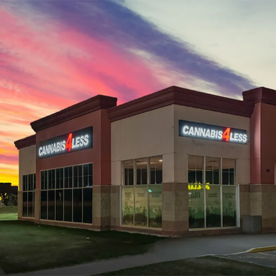 Cannabis 4 Less store exterior, lit sign, sunset sky background. Beige building, glass windows.