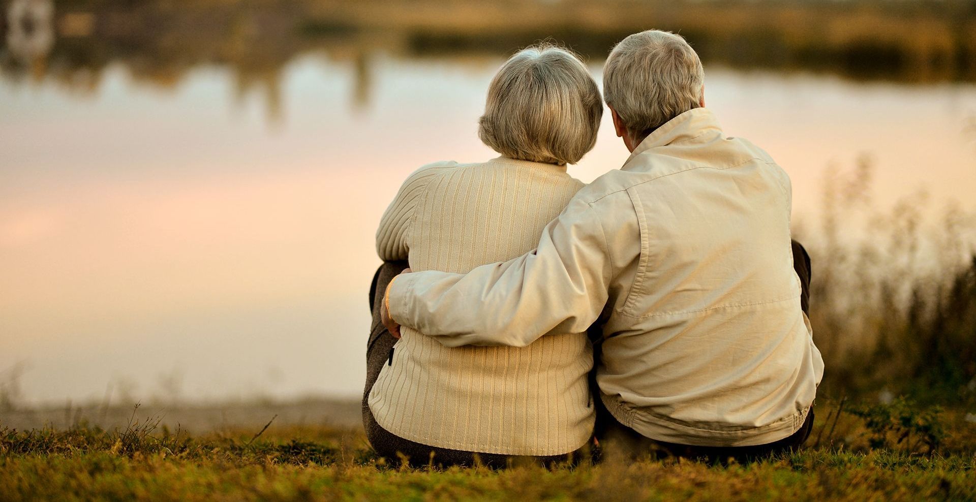 an elderly couple is sitting next to each other in front of a lake .