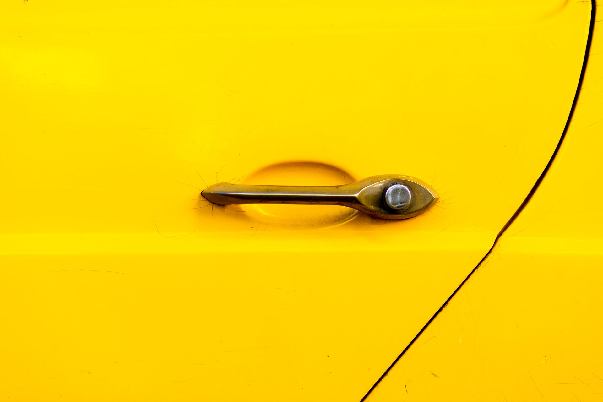 Close-up of a yellow vehicle door featuring a metal handle and surrounding panel.