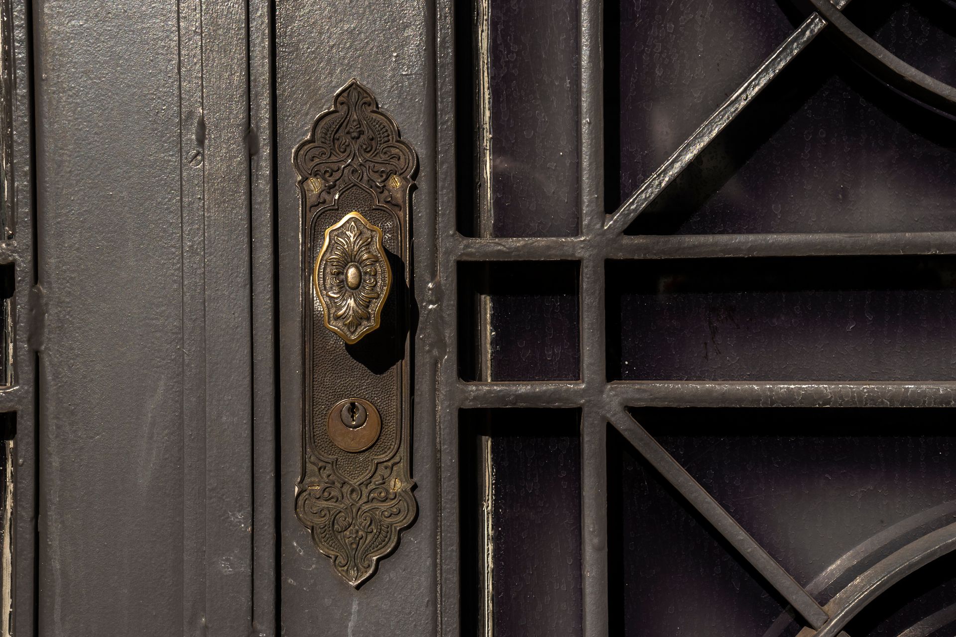 A close-up of a rustic metal door handle with an attached keyhole.