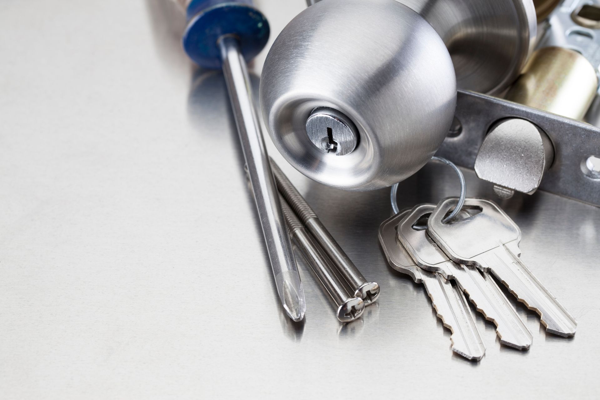 Close-up of door lock, keys, and screwdrivers on metallic surface.