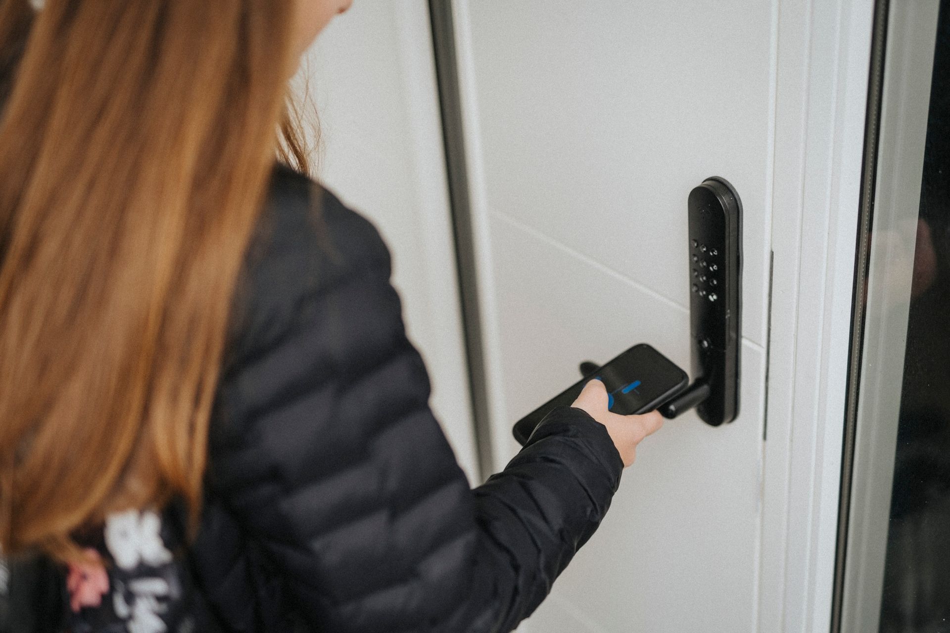Girl unlocking door lock through smart phone while standing at home.