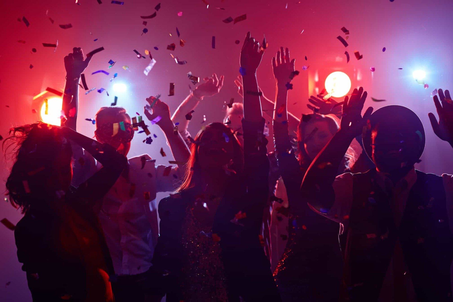 A group of people are dancing with their hands in the air amid confetti and colorful lighting on a Cedar Rapids party bus.