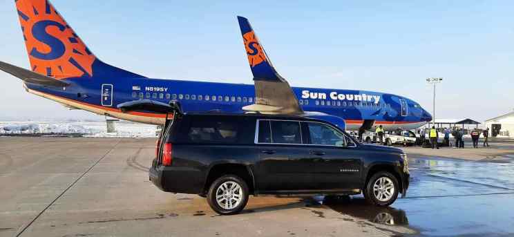 A black Chevrolet Suburban SUV is parked on an airport tarmac, with a Sun Country Airlines airplane in the background and several people standing nearby, exemplifying CID airport private transportation at its finest.
