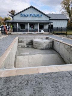 A swimming pool is being built in front of a building that says s & s pools.