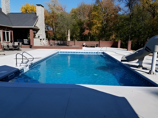 A large swimming pool with a slide and a house in the background