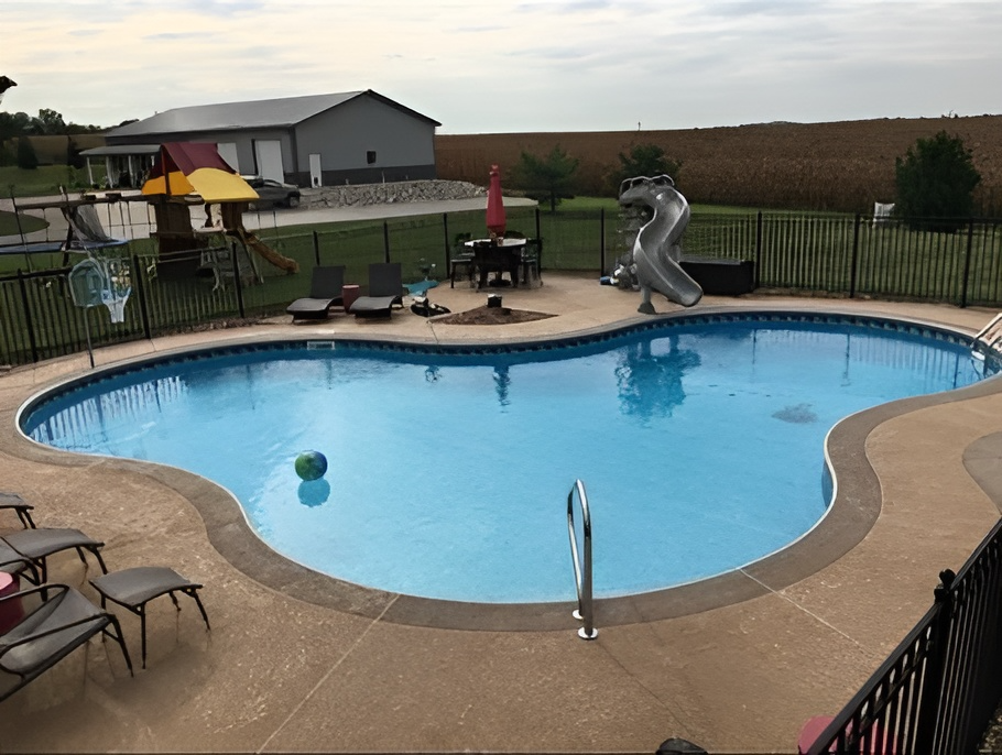 A large swimming pool with a slide and a playground in the background.