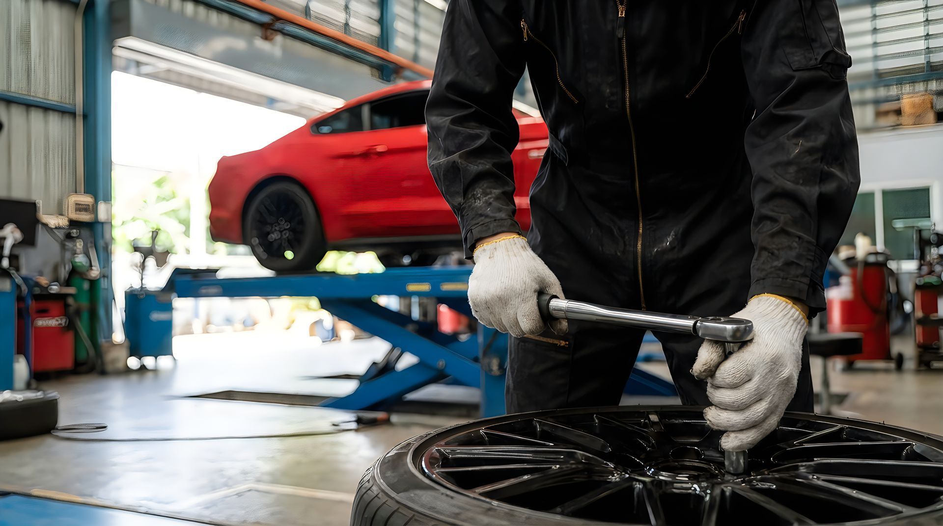 Auto shop technician in gloves working on a tire and wheel assembly in a service bay