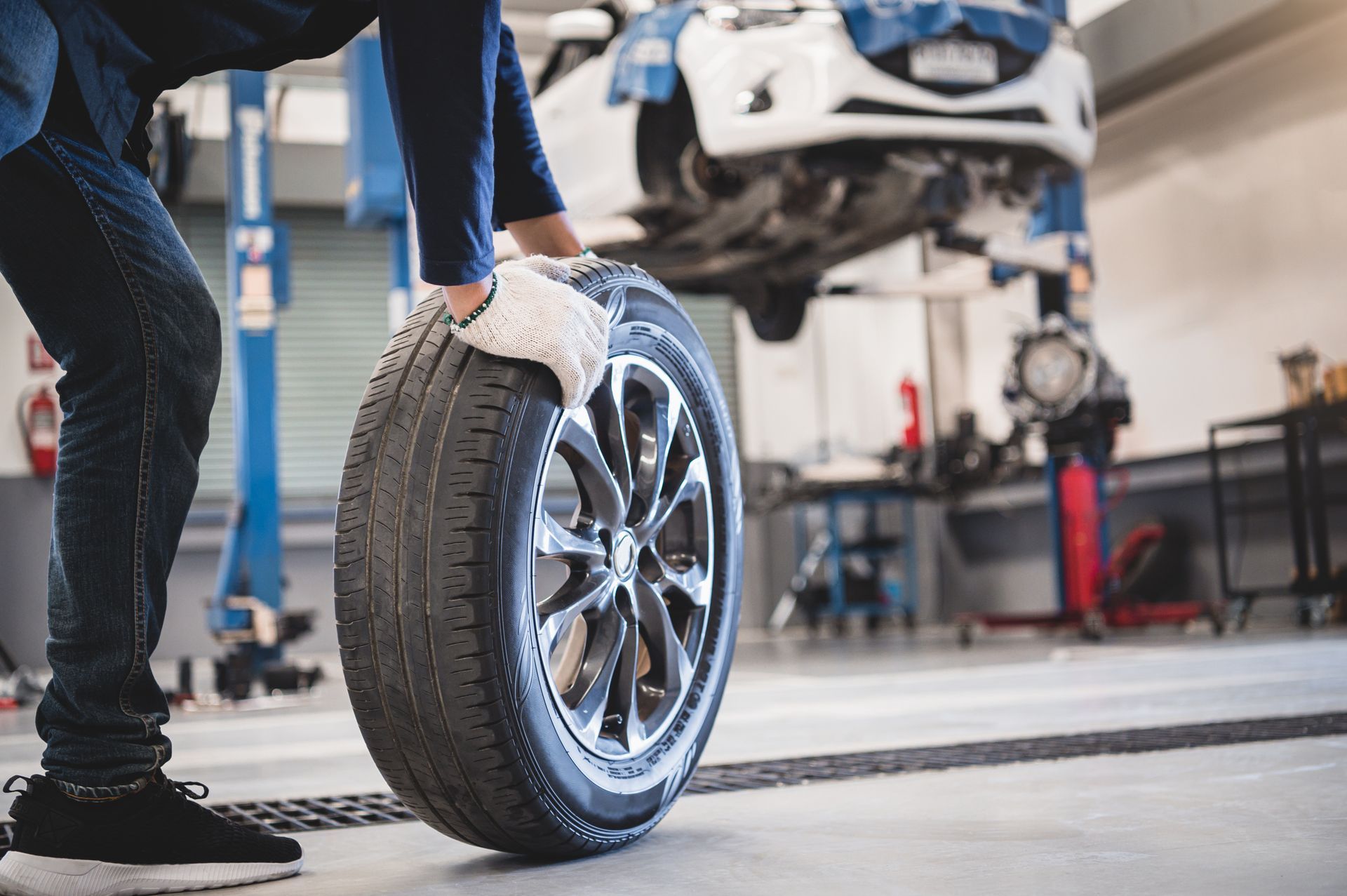 A mechanic holds and rolls a tire at a tire shop. A mechanic holds and rolls a tire at a tire shop.
