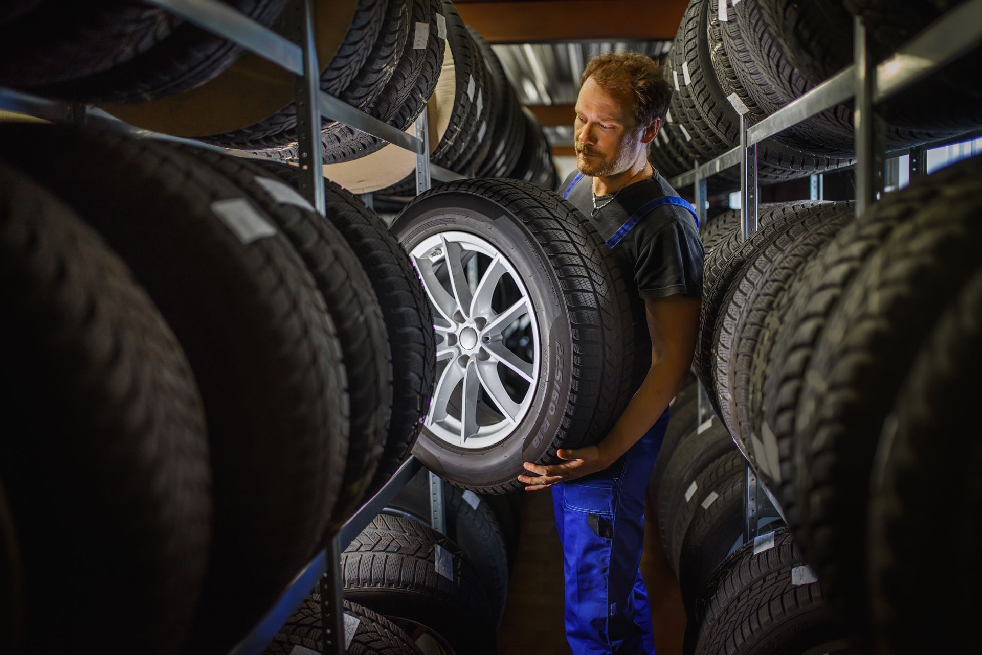 Auto shop technician selecting a tire from shelves of inventory in a tire service center