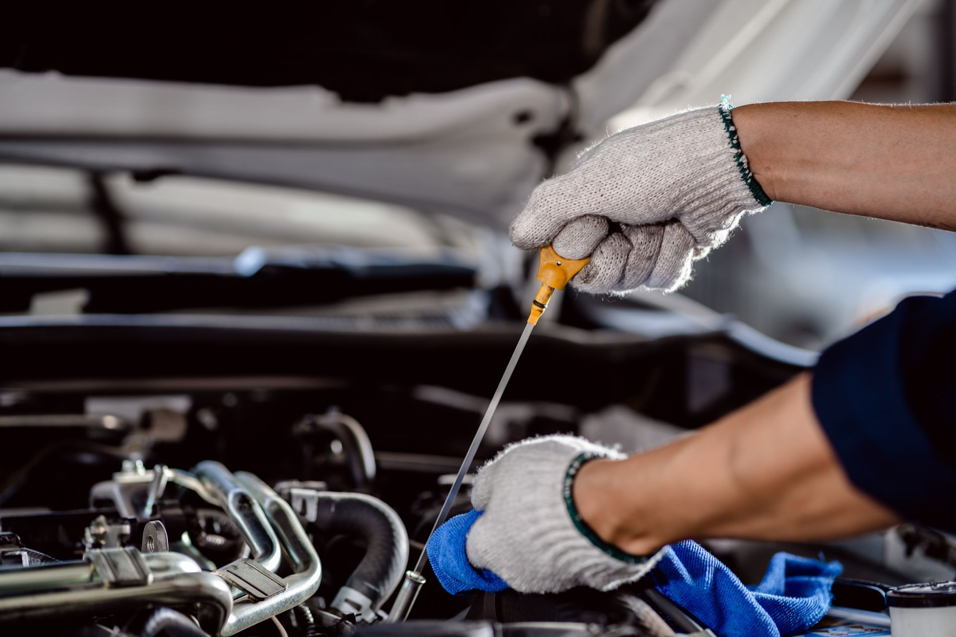 Mechanic in gloves checking engine oil level with a dipstick under an open hood Mechanic in gloves checking engine oil level with a dipstick under an open hood