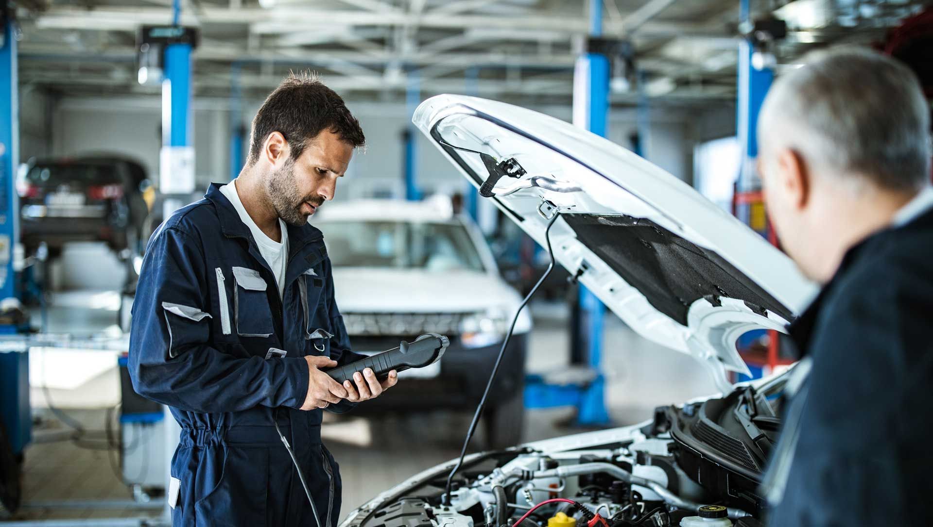 Young mechanic using a diagnostic tool to analyze car performance in a workshop.