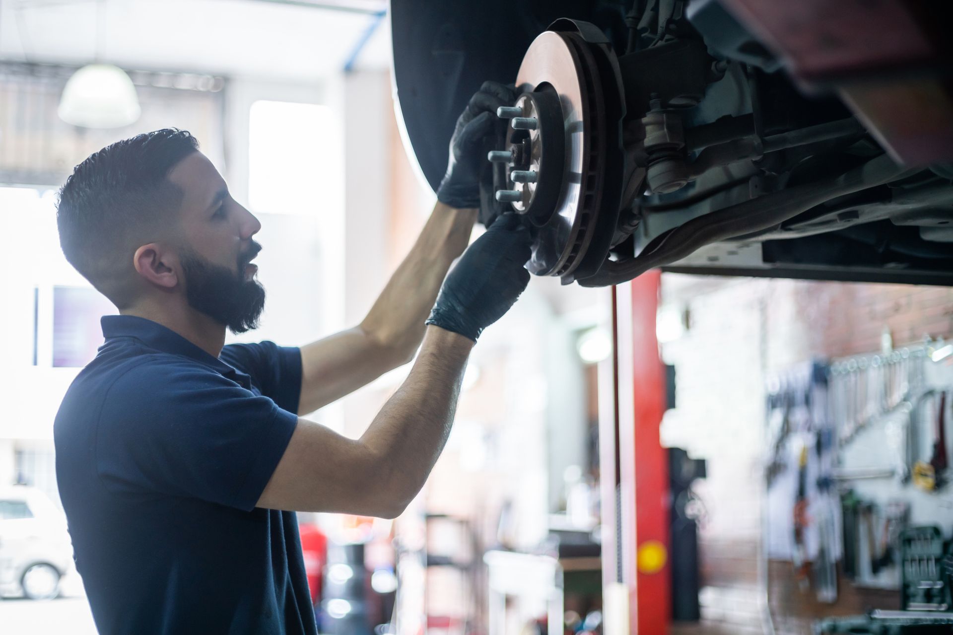 Male mechanic checking the brake disk of a car on lift, showcasing expert brake services.