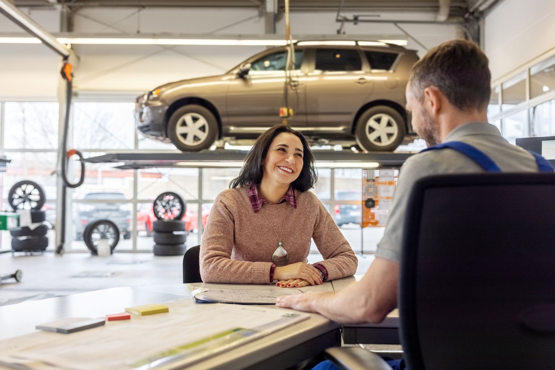 Woman talking with auto repair shop worker sitting in office
