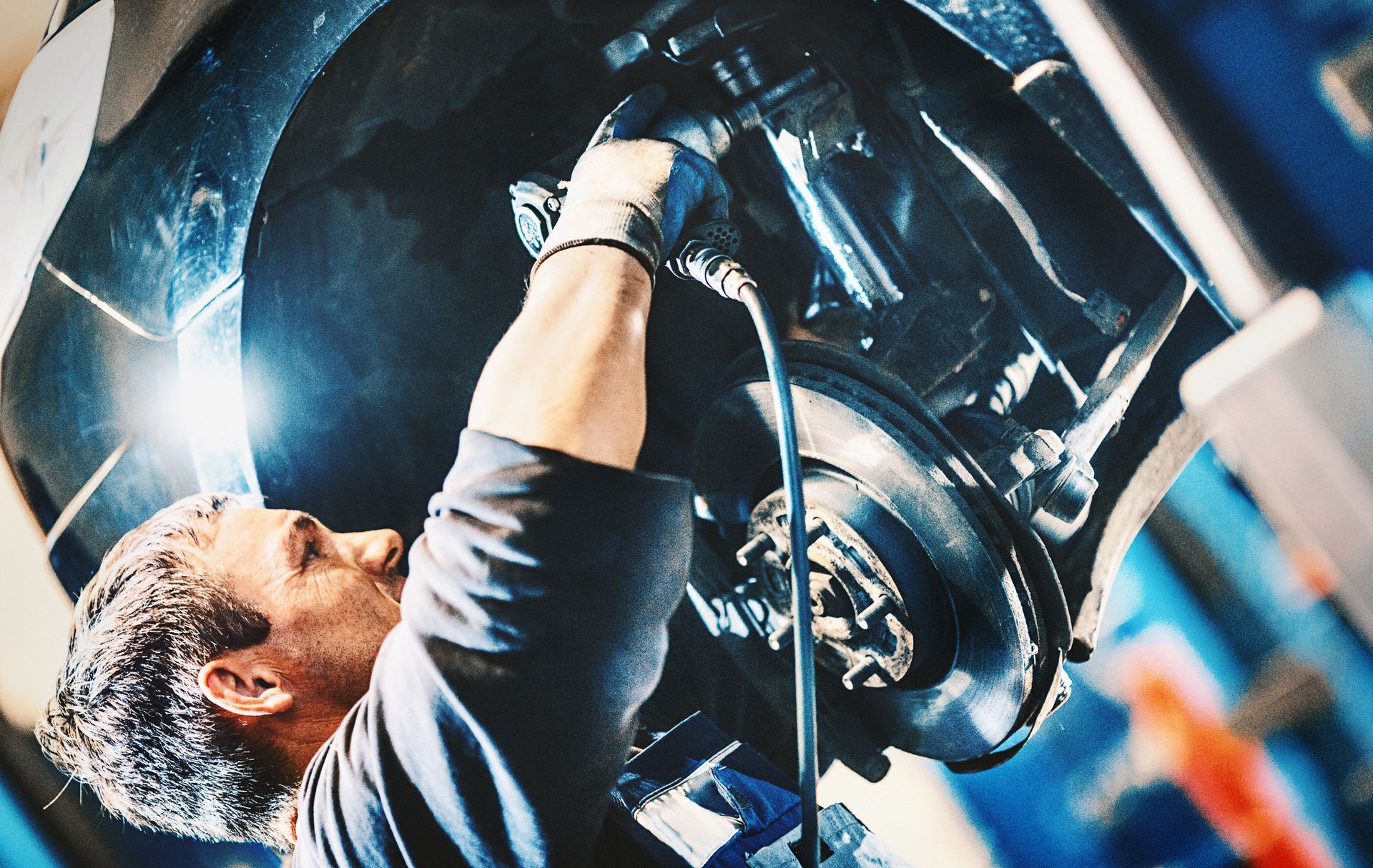 Mechanic using pneumatic tool to repair car brake system inside professional auto repair shop.