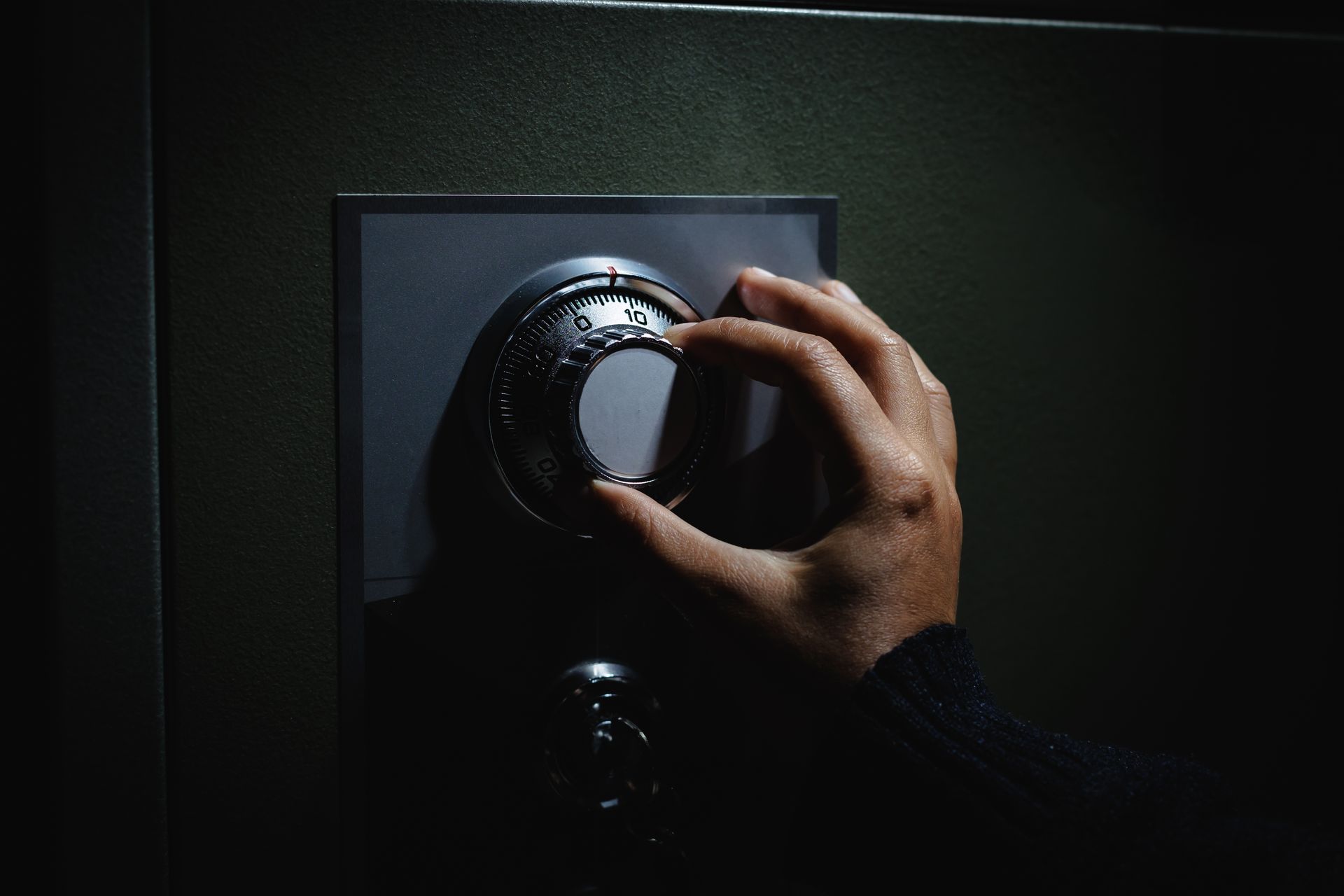 A hand turns the dial of a dark-colored safe in dim lighting.