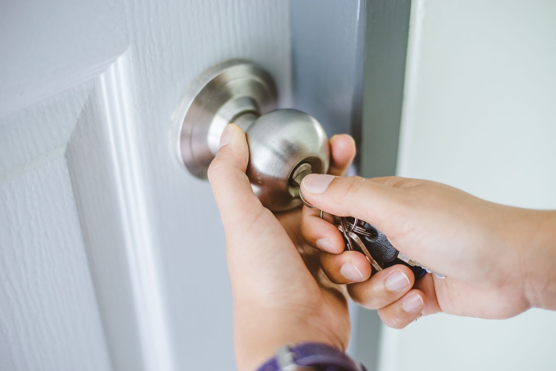 Hands inserting a key into a metal door knob on a white door.