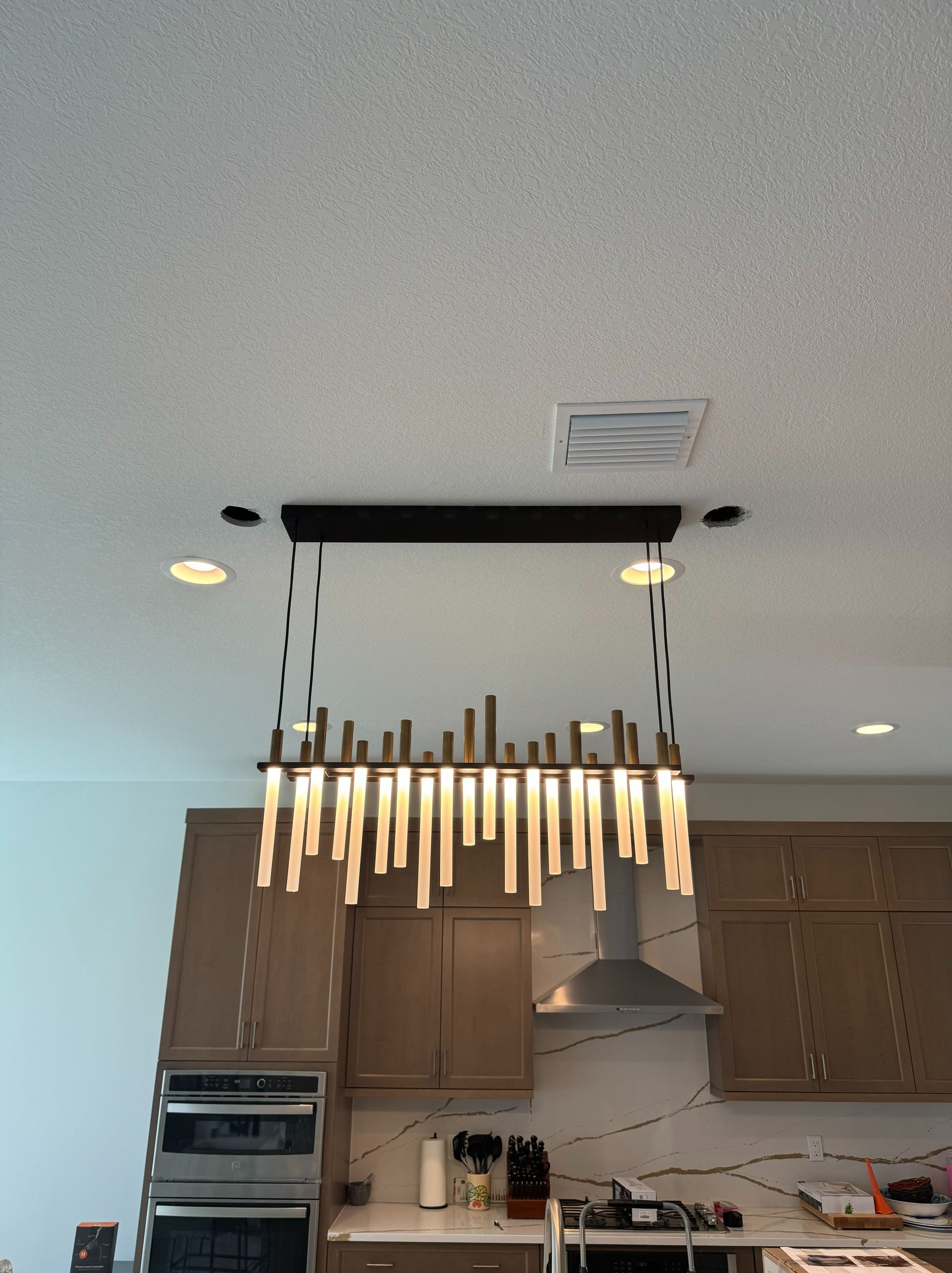 A modern kitchen chandelier with hanging light fixtures over a kitchen island, near cabinets and an oven.