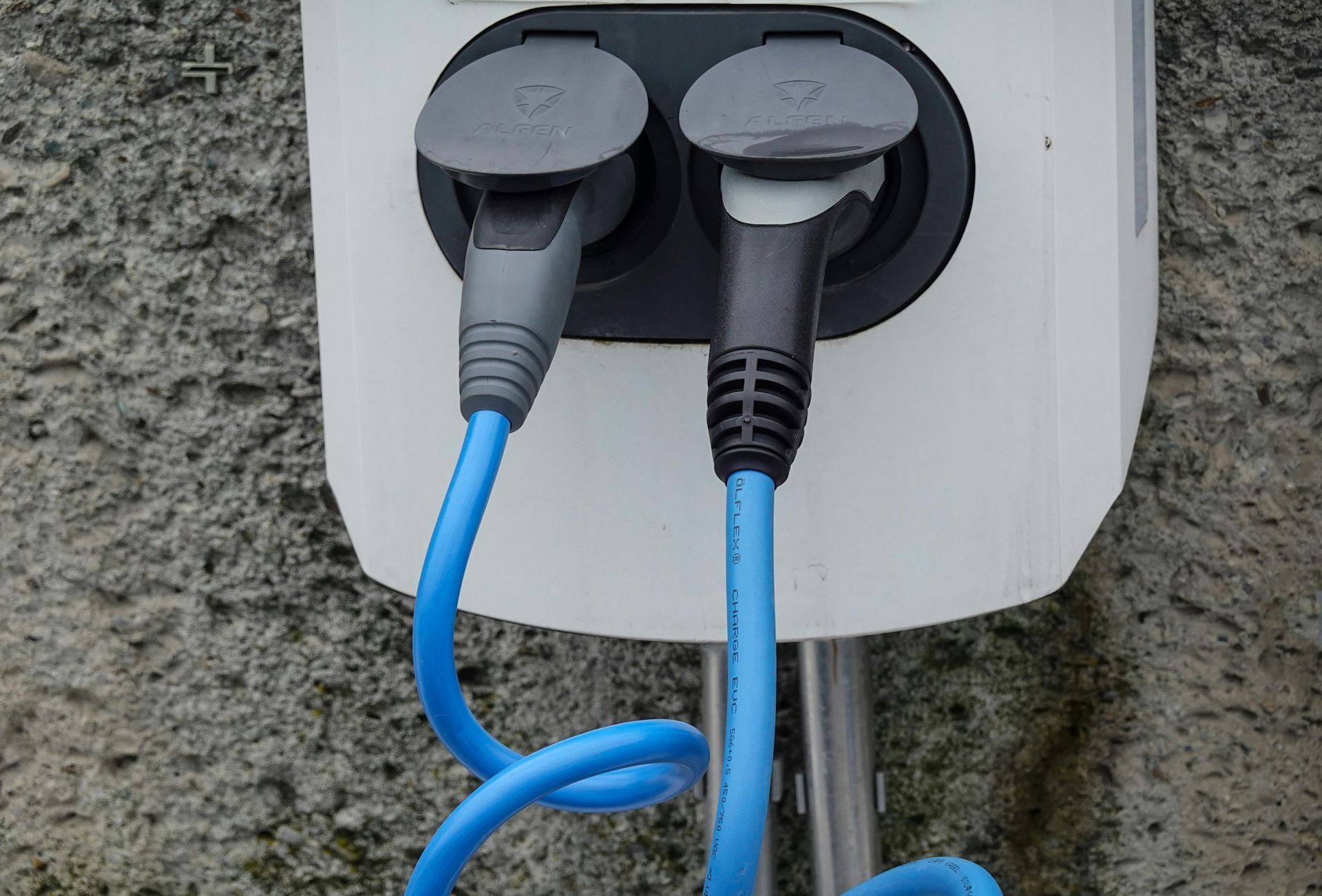 Two EV charging cables plugged into a white wall-mounted charging station, blue cables.